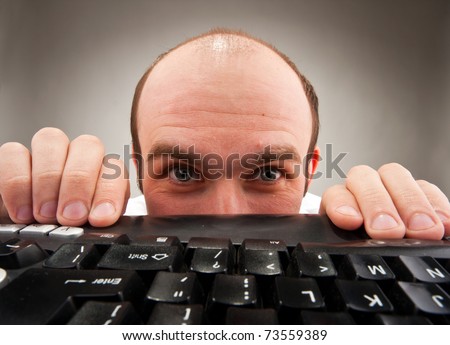 Timid nerd hiding under computer keyboard. Wide angle