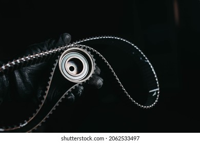 timing belt and tension roller in the hand of an auto mechanic on a black background, the concept of scheduled maintenance of the car, replacing the timing belt.