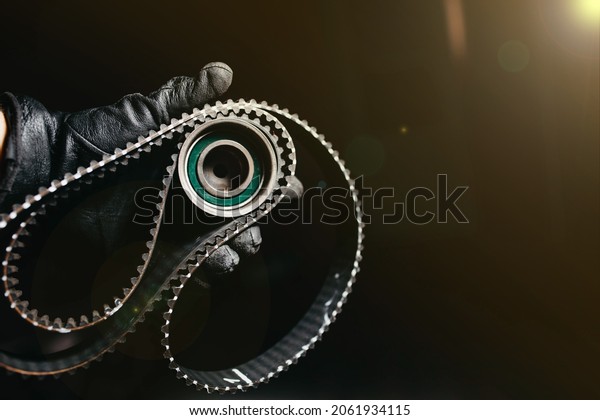 timing belt and tension roller\
in the hand of an auto mechanic on a black background, the concept\
of scheduled maintenance of the car, replacing the timing\
belt.