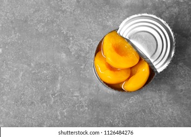 Tin can with conserved peaches on grey background, top view