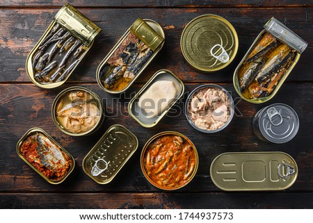 Tin cans for fish with different types of seafood, opened and closed cans with Saury, mackerel, sprats, sardines, pilchard, squid, tuna, over dark wood old table flatlay top view