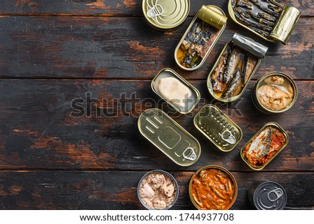 Tin cans for fish with different types of seafood, opened and closed cans with Saury, mackerel, sprats, sardines, pilchard, squid, tuna, over dark wood old table flat lay top view space for text