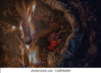 Tin Foil Wrapped Potatoes Cooking By The Side Of Bonfire During Camping. Long Exposure Shot Of Fire