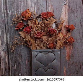 A Tin Hole Punched Container With Dried Flowers Against A Weathered Background