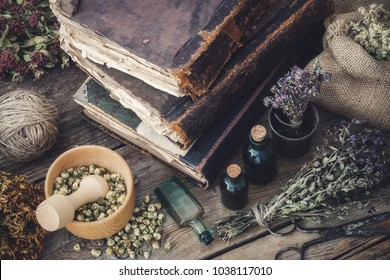 Tincture bottles, assortment of dry healthy herbs, old books, mortar, scissors on old wooden desk. Herbal medicine. Top view.