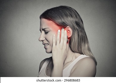 Tinnitus. Closeup up side profile sick female having ear pain touching her painful head temple isolated on gray wall background