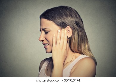 Tinnitus. Closeup side profile sick young woman having ear pain touching her painful head isolated on blue background