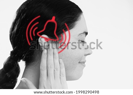 Tinnitus. A dissatisfied young woman holds her hand over her ears, experiencing ringing and pain. The concept of ear diseases and deafness.