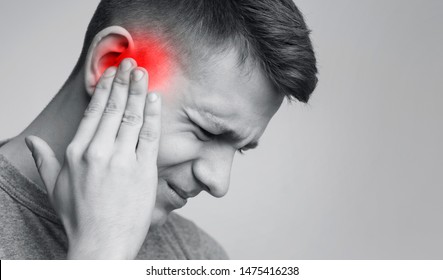 Tinnitus. Sick man having ear pain, touching his painful head, monochrome photo with red spot, free space