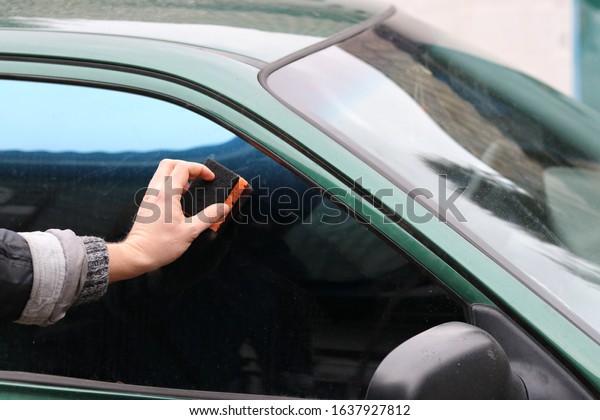 tinted car window. a man washes a car window\
with a washcloth.
