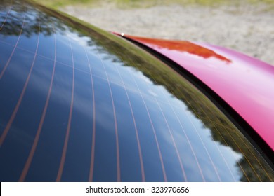 Tinted Window On A Red Car. An Image Of A Tinted Rear Window On A Red Modern Car. Image Is To Show The Blackness With A Reflection From The Forest. Focus Point Is In The Window Surface In The Front.