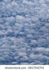 A tiny airplane flying through a beautiful cloudy blue sky