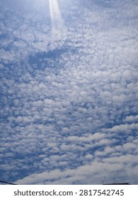 A tiny airplane flying through a beautiful cloudy blue sky
