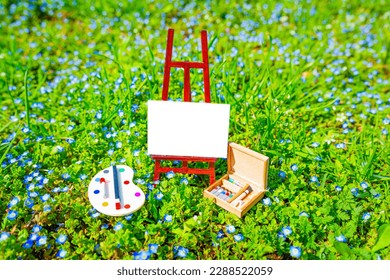 Tiny blank canvas on a small wooden stand, miniature palette and paint set nestled in a lush green field. Hello spring concept. - Powered by Shutterstock