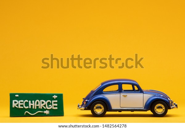 Tiny blue
car figurine aligned to the right next to a green sign with the
word recharge on it, on orange
background.