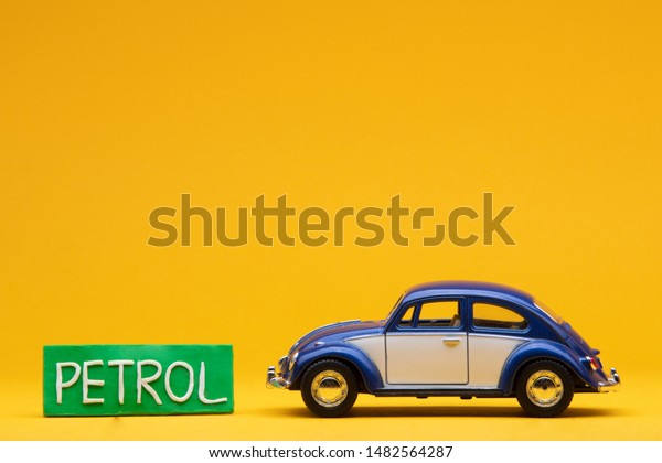 Tiny\
blue car figurine aligned to the right next to a pale green sign\
with the word petrol on it, on orange\
background.