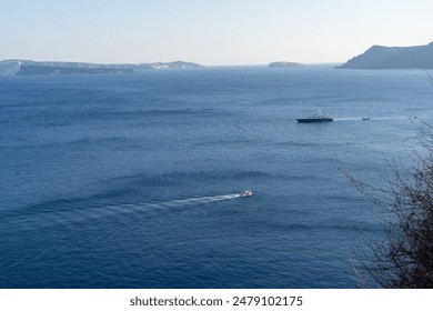 A tiny boat passing by two smaller boats amidst ocean and mountains