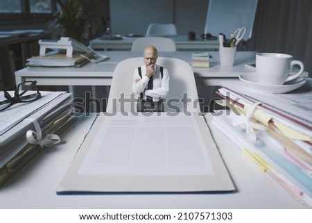 Tiny businessman checking a huge business contract, he is thinking with hand on chin