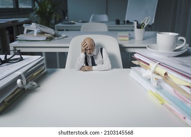 Tiny businessman sitting at office desk and thinking, he is desperate and exhausted, blank copy space