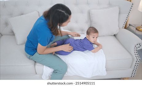 A tiny child happily on the sofa waiting for mother put on clothes