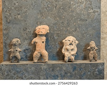 Tiny clay figures stand on a weathered stone ledge. Each figure shows distinct postures and expressions. They appear ancient, handcrafted with care and intention. Their surfaces are worn