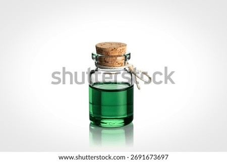 A tiny clear glass bottle filled with vibrant green liquid, sealed with a natural cork stopper and a small white string.
