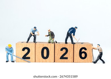 Tiny construction worker figurines working on wooden blocks showing the number 2026, symbolizing progress and the future.