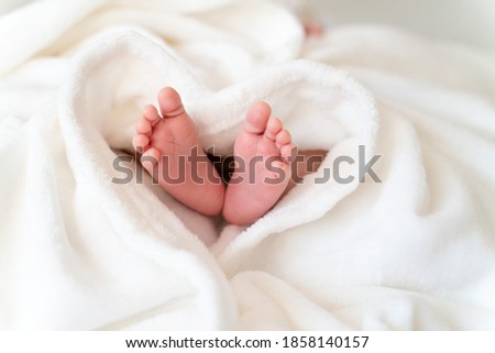 tiny, cute, bare feet of a little caucasian newborn baby girl/boy wrapped in a heart shaped white soft and cosy blanket, symbolizing love  