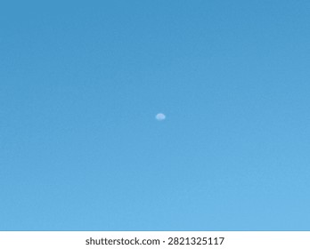 Tiny, Distant Object Daytime Moon Against a Clear Blue Sky
A high-resolution photograph capturing a single, small, indistinct object positioned centrally against a vast and uniform expanse of clear blue sky during the daytime.