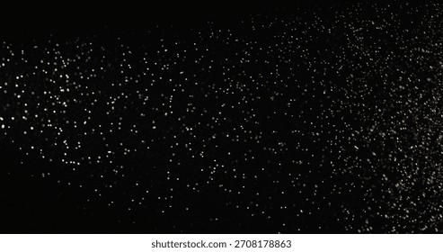 Tiny dust particles fly randomly in the smoky air, an empty template of space for objects. Many glittering particles of powder fall onto an empty black contrasting background in the rays of light.
