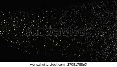 Tiny dust particles fly randomly in the smoky air, an empty template of space for objects. Many glittering particles of powder fall onto an empty black contrasting background in the rays of light.