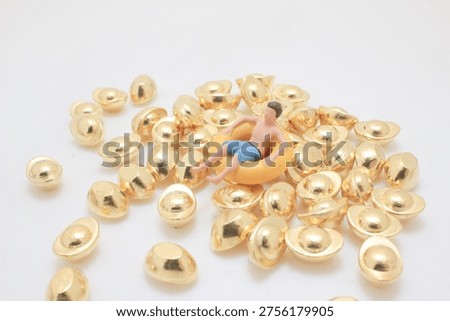 Tiny figurine rests in inflatable ring atop shiny gold pieces