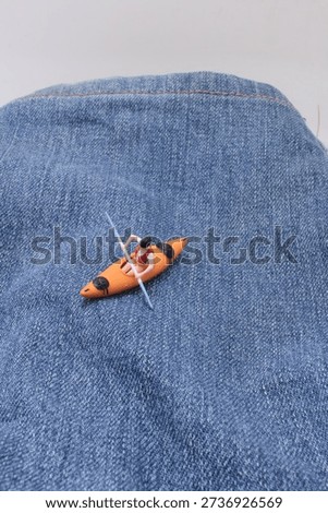 Tiny figurine rows orange kayak atop blue jeans