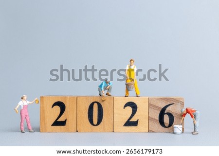 Tiny figurine workers painting and assembling wooden blocks to form the number 2026, symbolizing preparation, planning, and new beginnings.