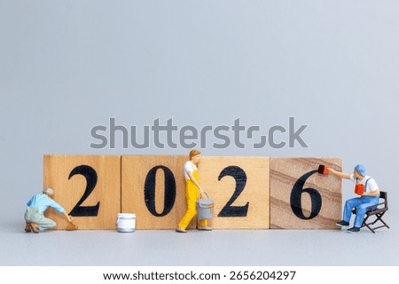 Tiny figurine workers painting and assembling wooden blocks to form the number 2026, symbolizing preparation, planning, and new beginnings.