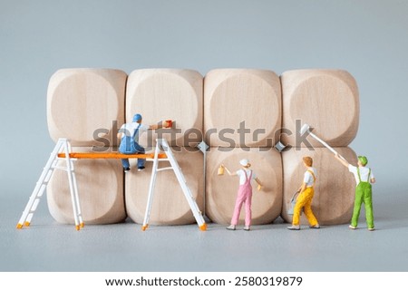 Tiny figurines dressed as painters creatively painting large wooden blocks, using ladders and scaffolding