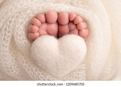 The tiny foot of a newborn baby. Soft feet of a new born in a white wool blanket. Close up of toes, heels and feet of a newborn. Knitted white heart in the legs of a baby. Macro photography. 