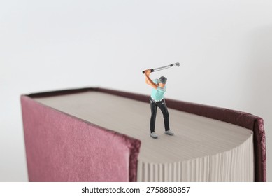 Tiny golf figure poses mid swing atop large book