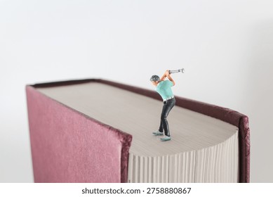 Tiny golf figure poses mid swing atop large book