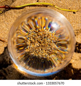 Tiny Grains Of Brightly Coloured Sand Viewed, Magnified And Sharp Focussed Through A Solid Glass Ball Placed On The Beach. Different Colours From Sedimentary Rock And Minerals.