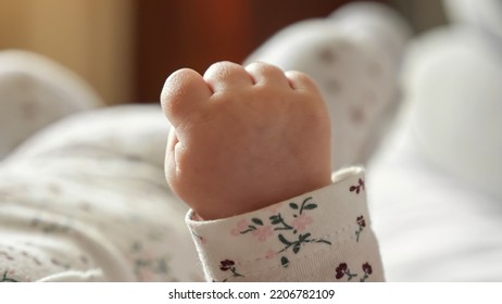 Tiny hand of newborn baby clenched into fist on blurred background in bedroom. Little baby girl relaxes lying on bed at home extreme close view