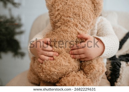 Tiny hands hug a fluffy teddy bear, a tender image of childhood innocence, comfort, and a beloved toy.