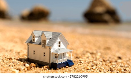 Tiny house sits on sandy beach. Blue porch contrasts with warm tones. Rocks stand in soft, blurry background. Sunlight glows gently across scene. This image captures peaceful, minimalist living