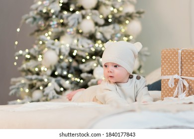 Tiny Little Child Celebrates Its First Christmas Among Gift Boxes And Christmas Lights. Christmas Eve At Home