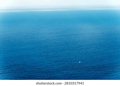Tiny lone sailboat surrounded by vast blue ocean and open water
Small distant sailboat alone in a vast blue ocean. Minimal sea scene symbolizing freedom, solitude, journey, distance and exploration.