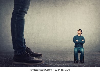 Tiny man employee seated on a chair looking up perplexed at his big boss. Office confrontation, motivation concept. Business person leadership concept. - Shutterstock ID 1754584304