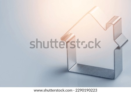 Tiny metal house on gray background. Could represent different ideas about real estate.