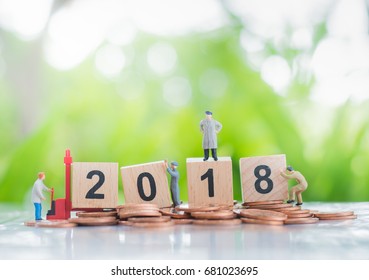 Tiny miniature model of working hard workers standing on a pile of coins and wooden number 2018 background using as investment, achievement and partnership business concept.