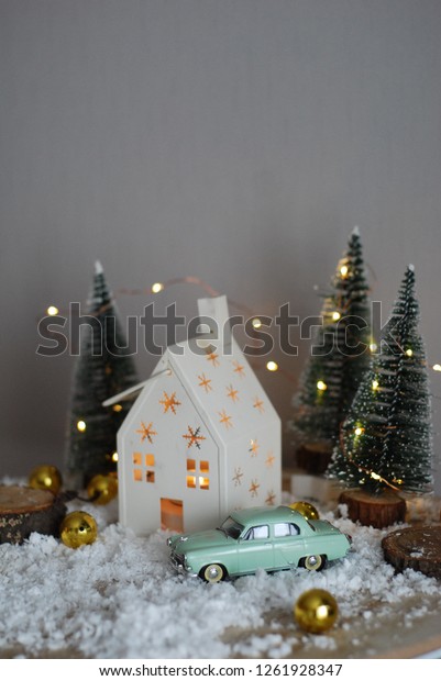 Tiny mint car near white house in christmas tree\
forest decorated with\
garlands