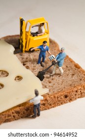 A tiny model figure of a foreman directs his miniature team in the making of a cheese sandwich using a forklift and loading equipment